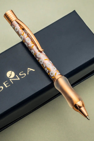 A rose gold pen with a delicate white and yellow floral pattern on its translucent barrel, featuring matching metallic accents.